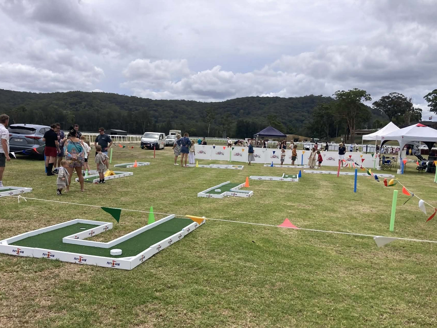 Miniature golf course with participants on a grassy field under a cloudy sky.