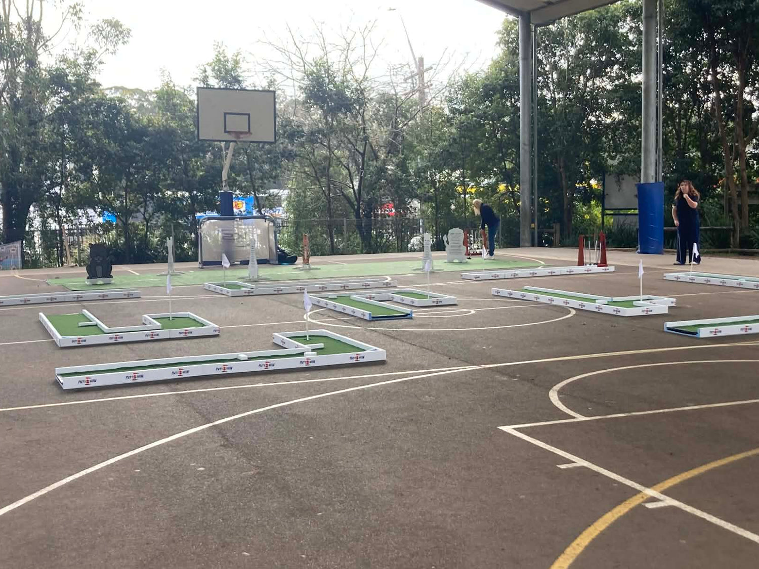 Outdoor basketball court with multiple hoops and a small sports field.